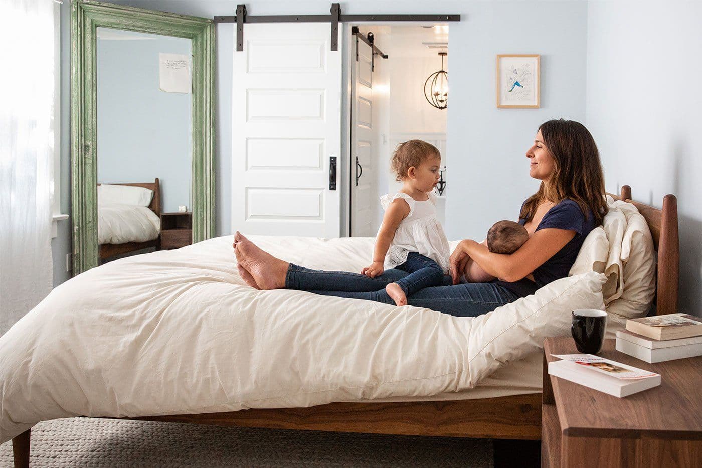 new mother breastfeeding newborn with toddler big sister on bed