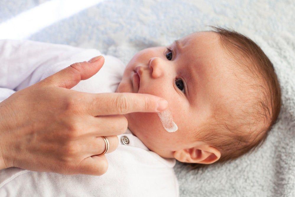 A parent applies lotion to their baby's cheek