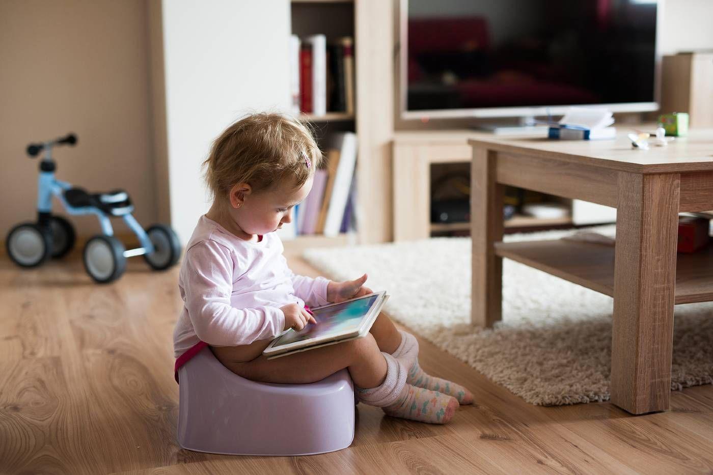 A constipated toddler sits on the potty with a book