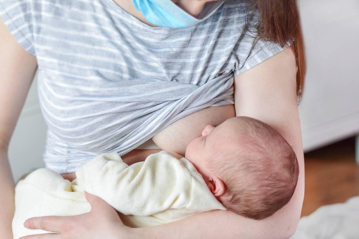 A mum breastfeeds her baby while wearing a mask