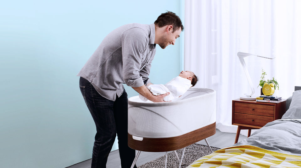 Father holding baby in arms above a Snoo Smart Sleeper Bassinet